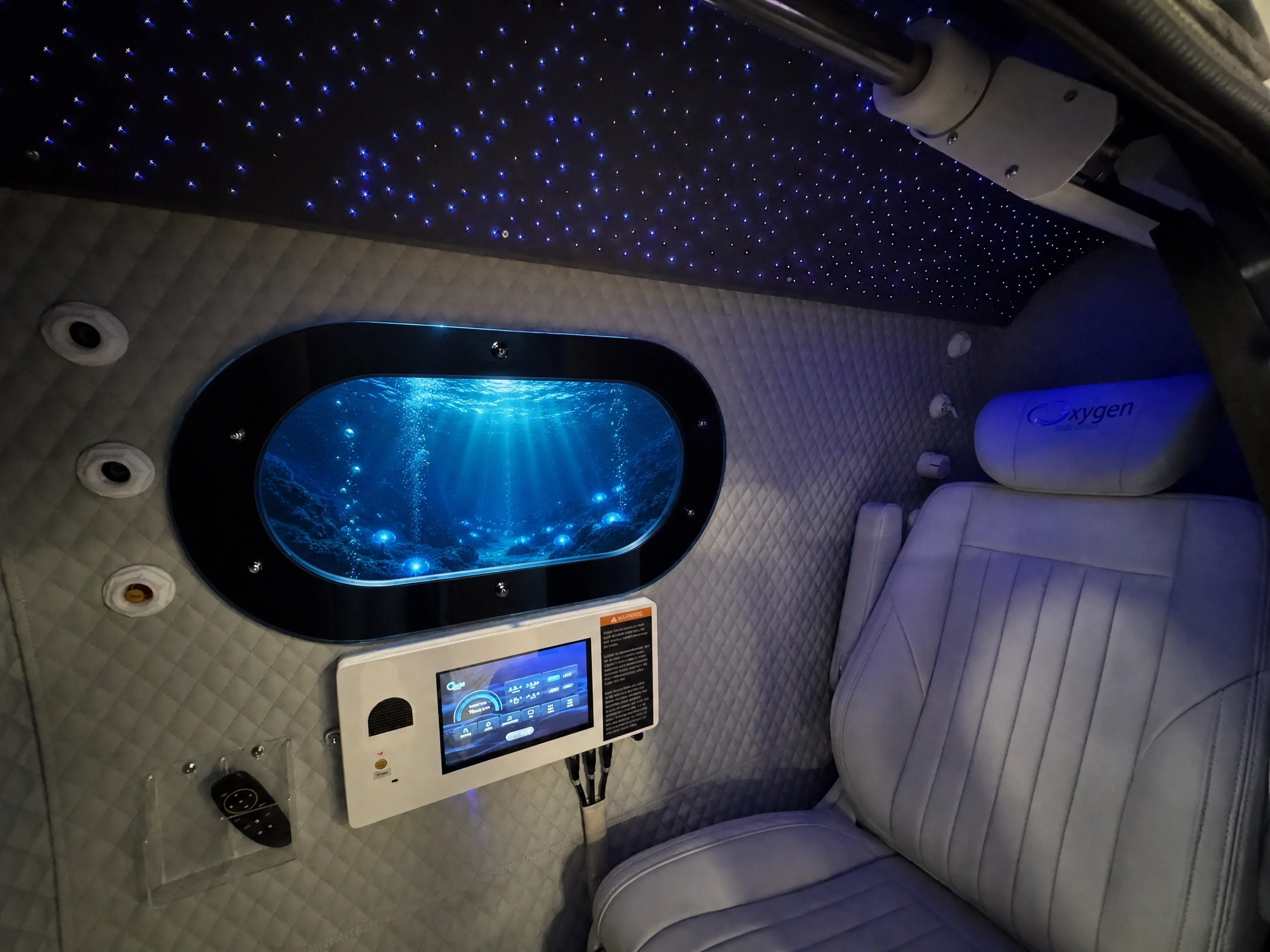 Interior of the Elite Comfort 34D with the starlight fiber-optic ceiling glowing above the quilted walls, the oval window showing an underwater ocean scene, the touchscreen control panel, and the premium reclining seat